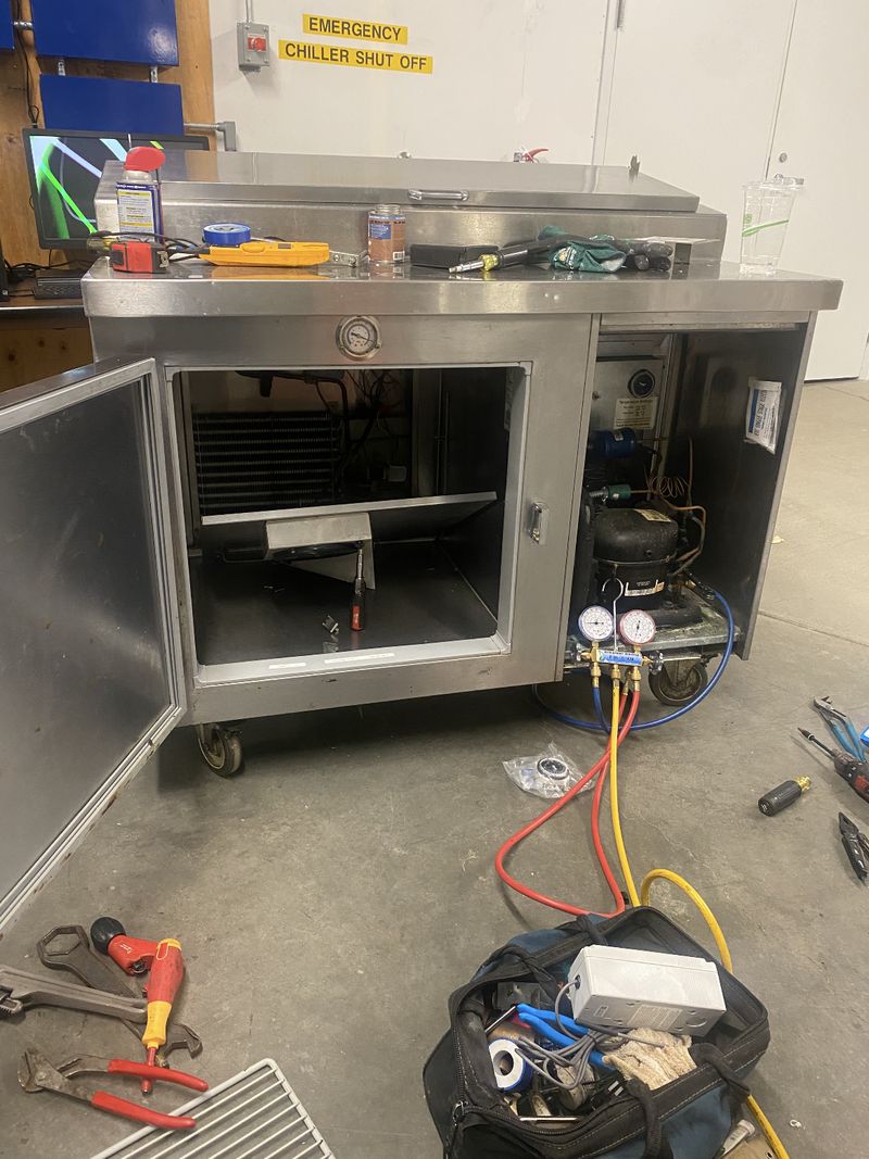 Commercial refrigerated prep table opened up with gauges attached to the compressor during repair